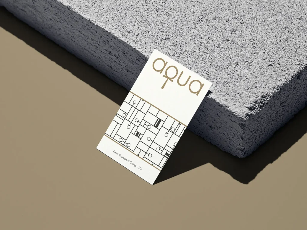 Minimalist restaurant business card on 18pt white uncoated stock, leaning against a grey concrete block and printed at our Manhattan shop.