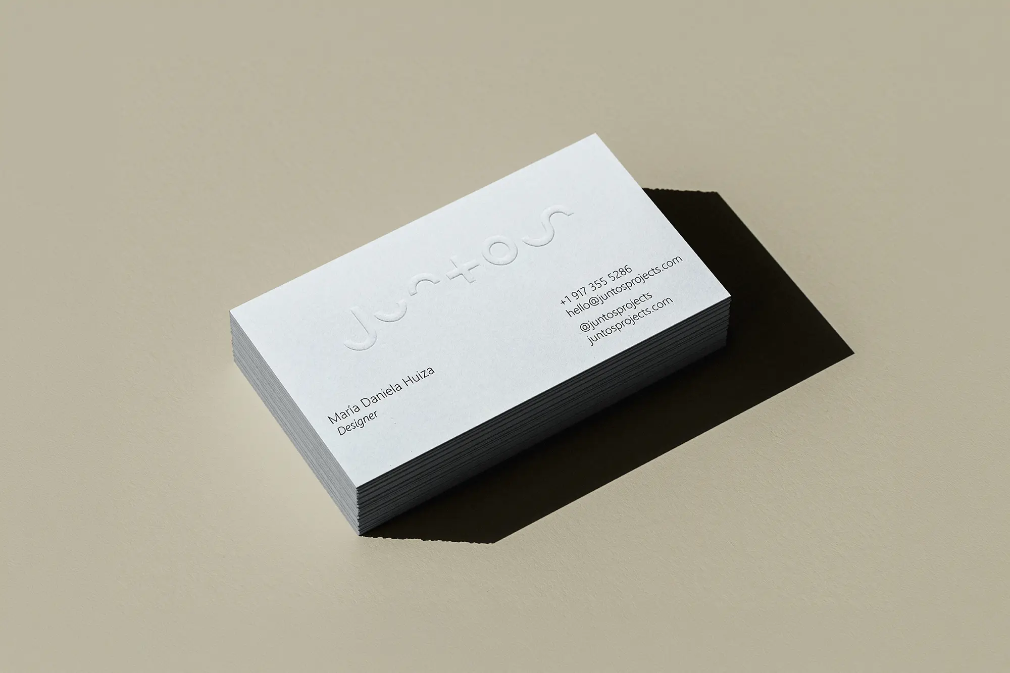 Close-up of a thick white business card for Juntos with a subtle blind embossed logo, showcasing the elegant "sculpted paper" effect that adds depth without the use of ink.