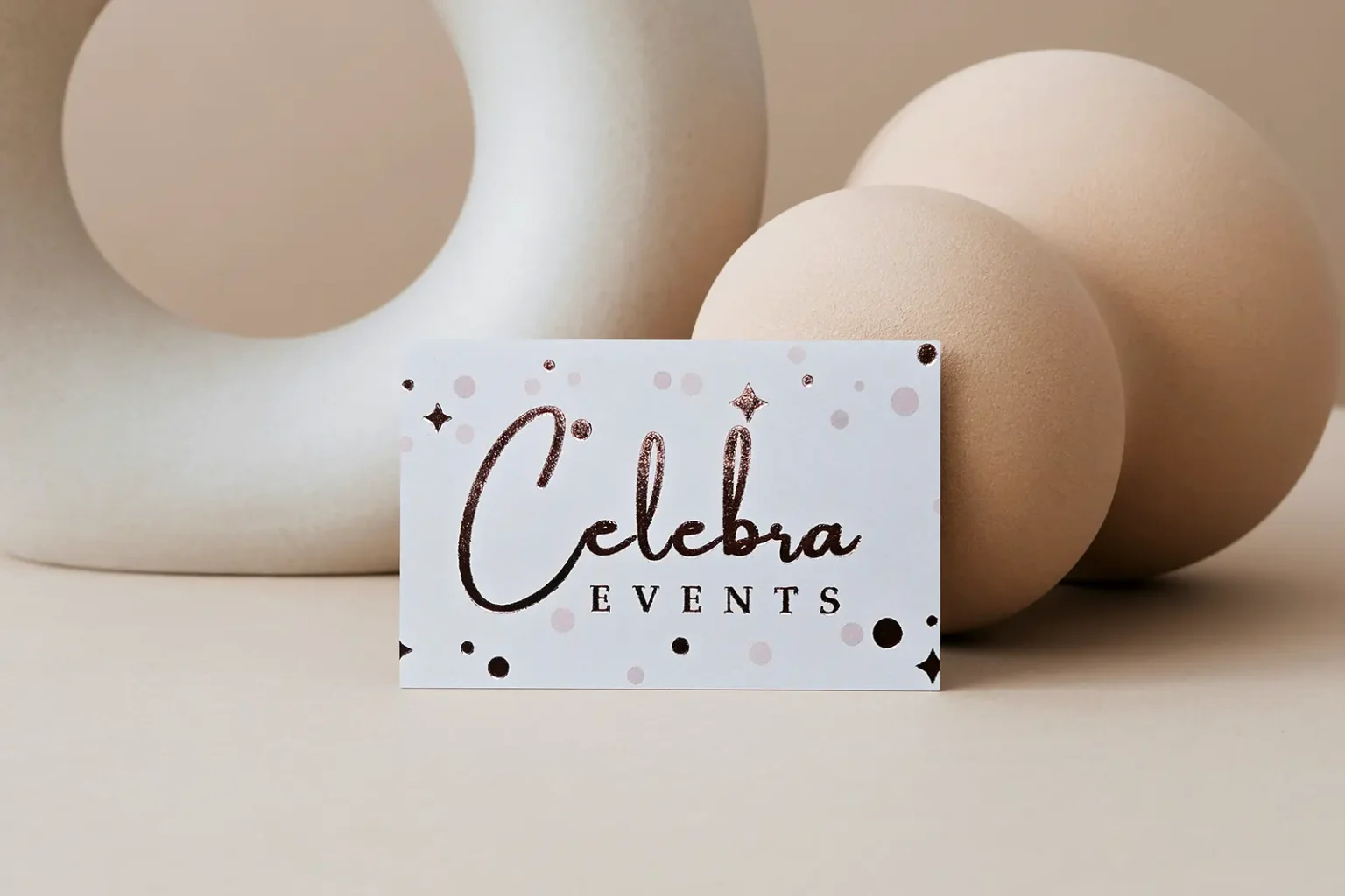 Stunning white business cards for Celebra Events with textured rose gold foil accents and star details, styled against modern neutral spheres.