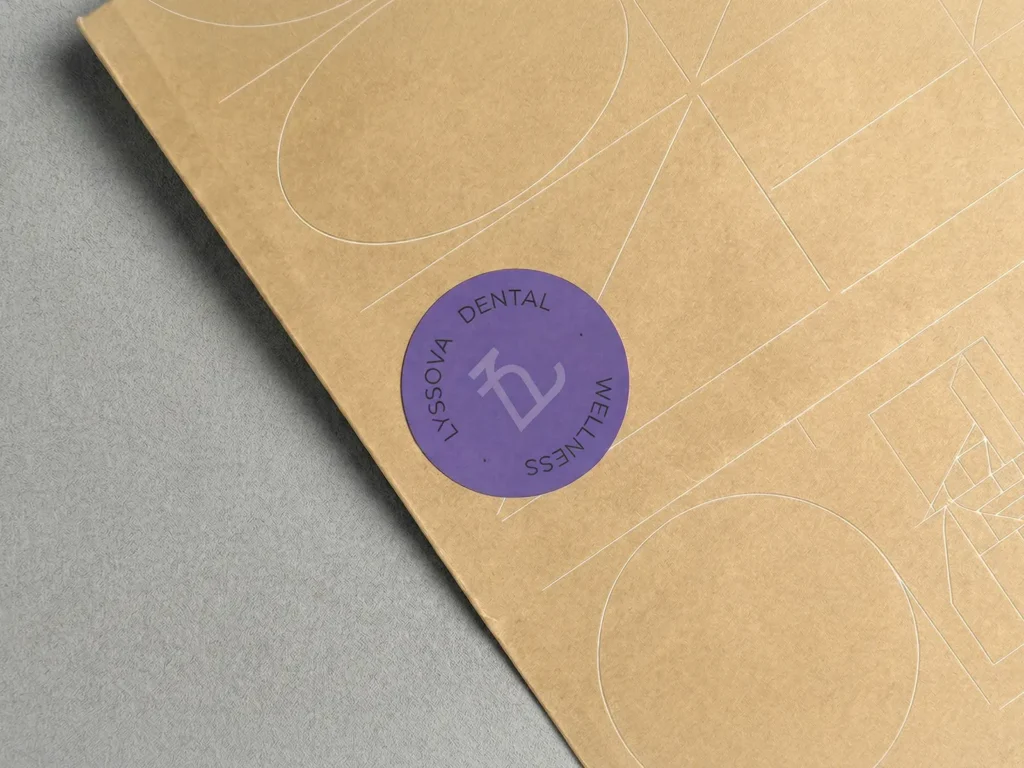 Custom purple vinyl stickers with a minimalist logo for a dental practice, printed on 70lb adhesive stock and shown on a brown kraft mailer.