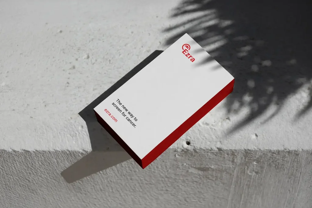 Minimalist white business cards for Ezra featuring striking red painted edges, stacked on a stone surface to emphasize the premium paper thickness.