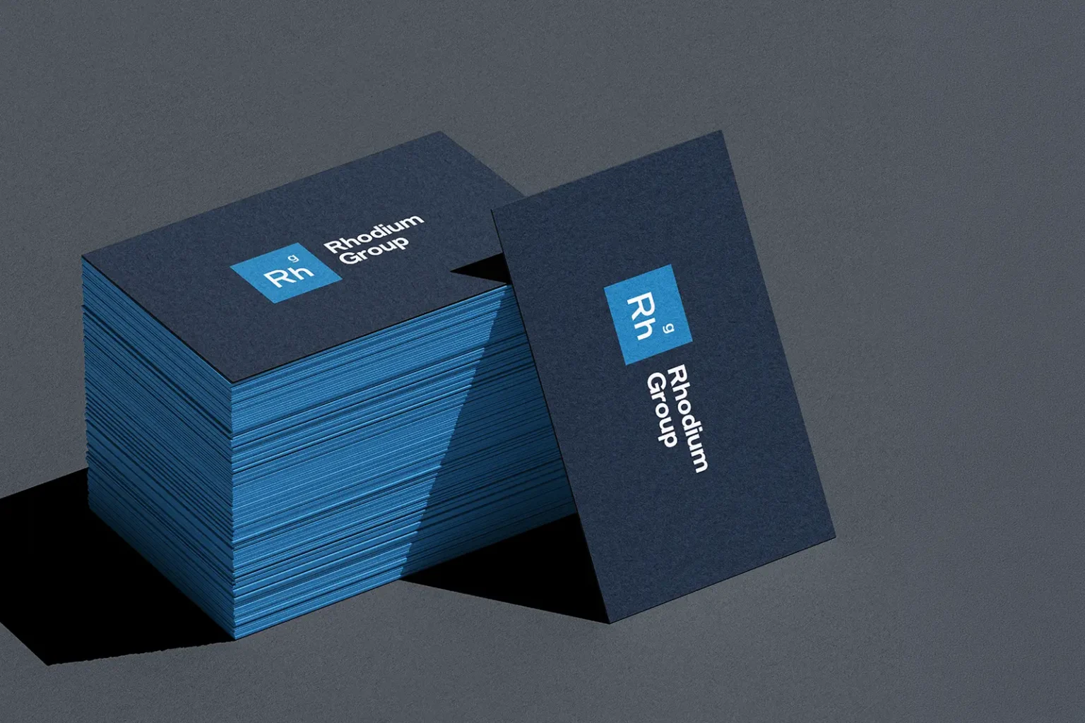 Deep navy Rhodium Group business cards with contrasting light blue colored edges, showcasing the precision of our NYC-based specialty printing services.