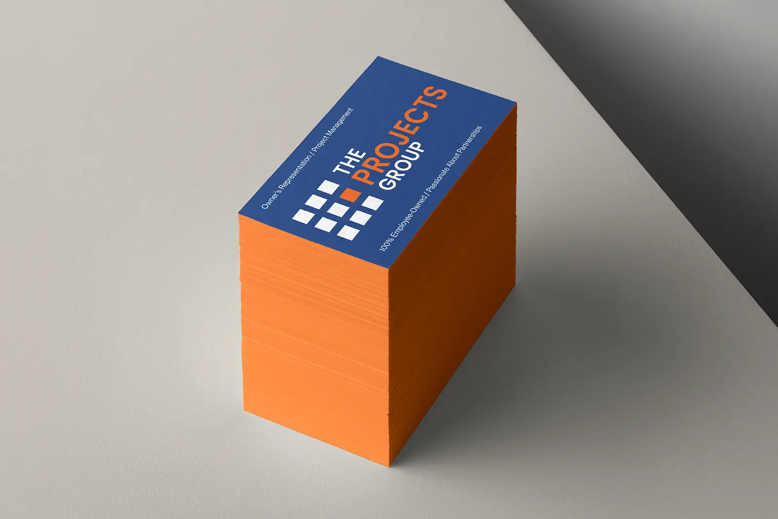 A tall stack of navy blue business cards for The Projects Group showcasing vibrant orange painted edges that provide a bold, high-contrast pop of color.