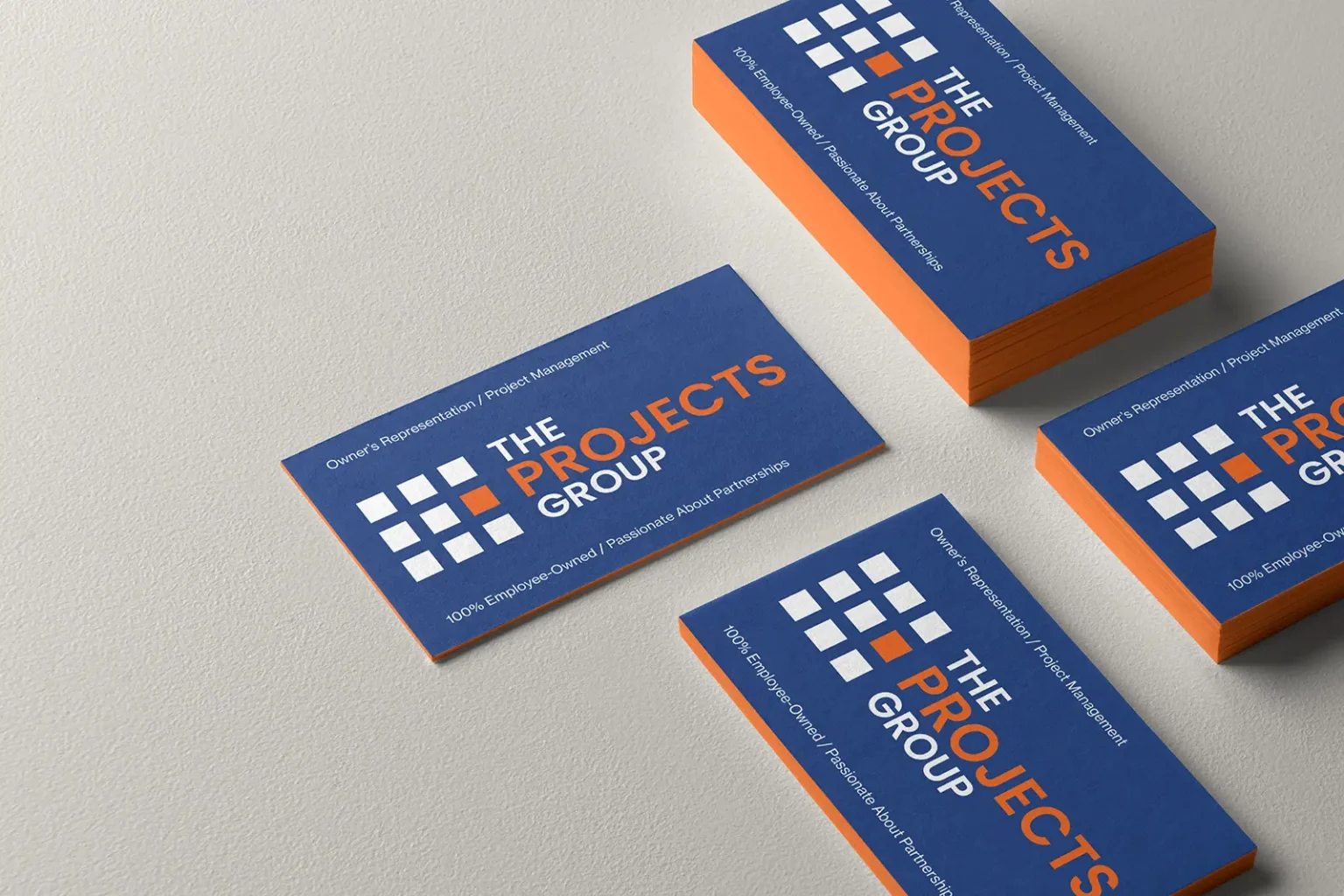 Multiple business cards for The Projects Group spread out on a table, showing off the consistent quality of our orange painted edges, locally printed in NYC.