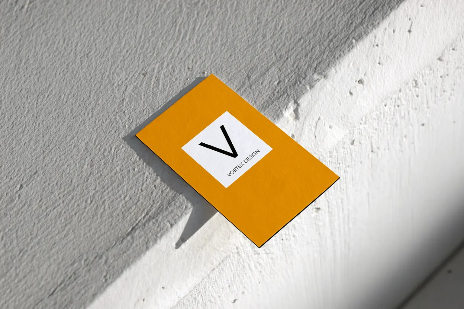A bright yellow Vortex Design business card leaning against a sunlit textured wall, highlighting the clean finish of our custom edge-painting process.