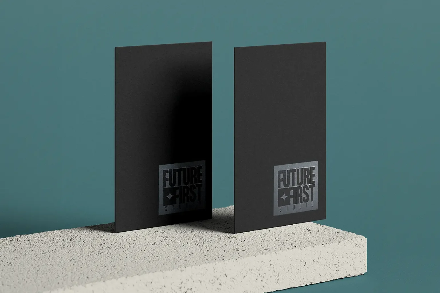Vertical matte black business cards for Future First Studio featuring a reflective spot gloss box logo, styled on a light concrete block.
