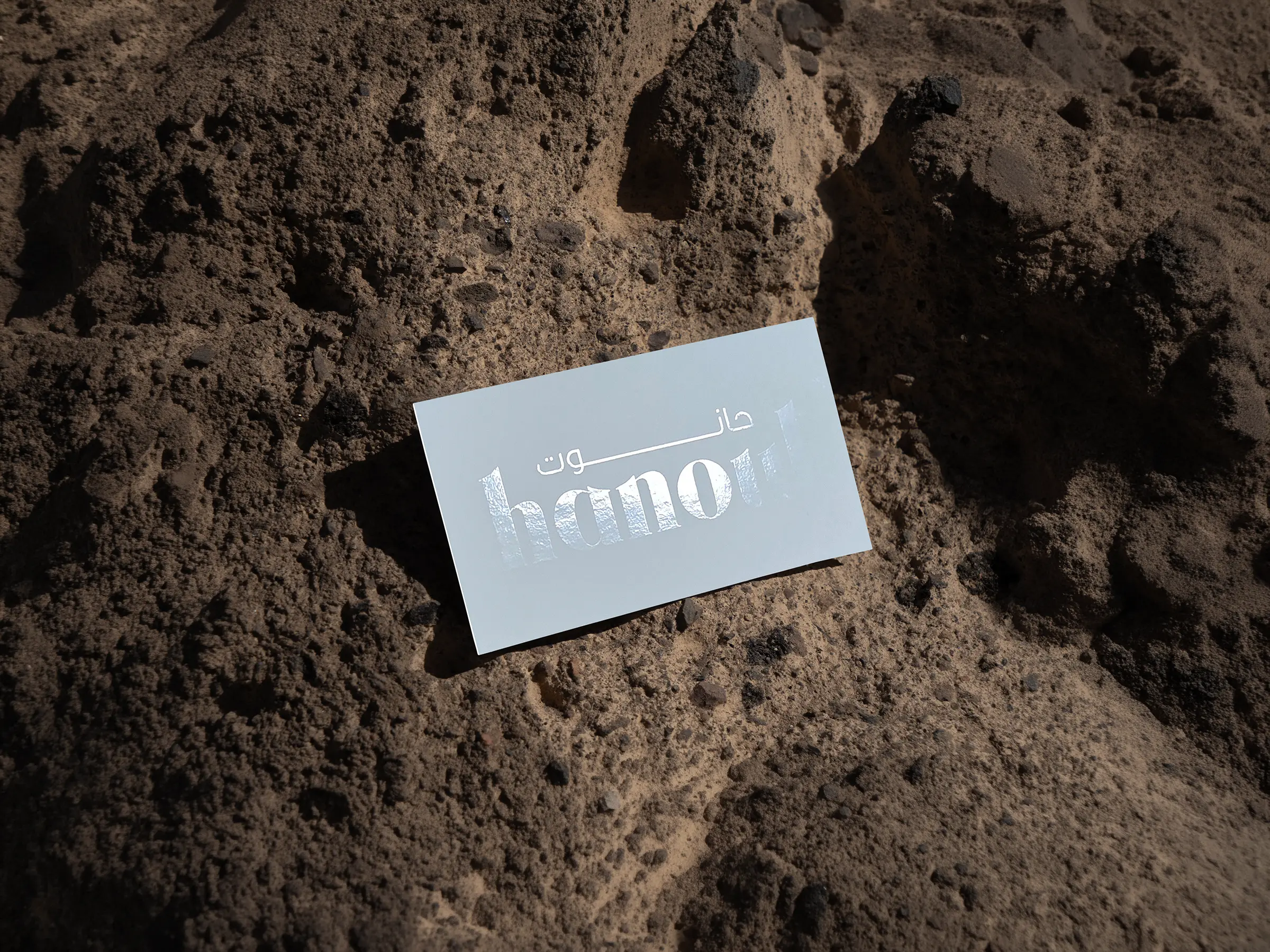 Custom white business card featuring bold spot gloss typography, displayed on a rugged stone surface and expertly printed at our NYC print shop.