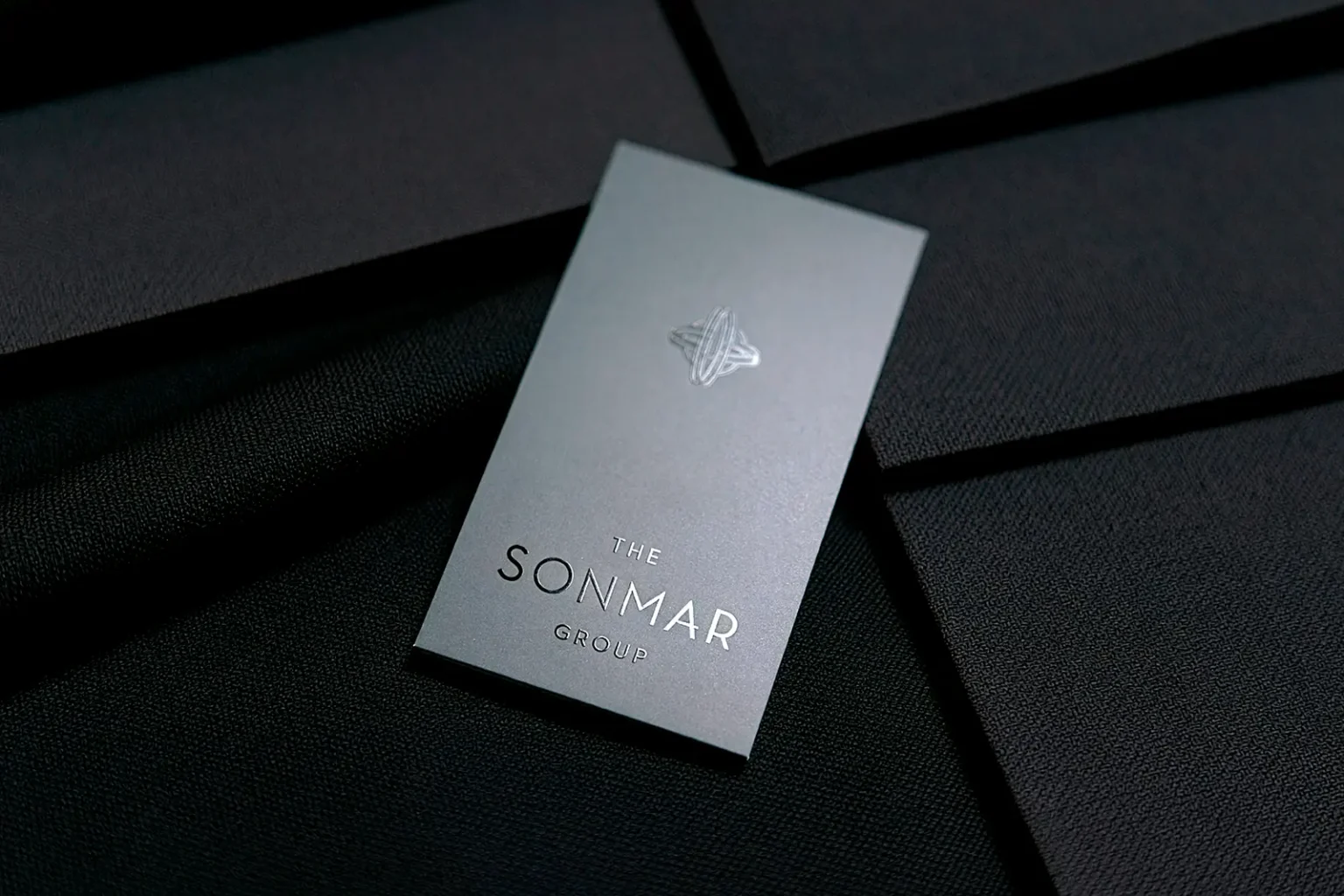 Luxury charcoal grey business cards for The Sonmar Group with an elegant spot UV emblem, showcasing the premium detail we provide for businesses across the five boroughs.