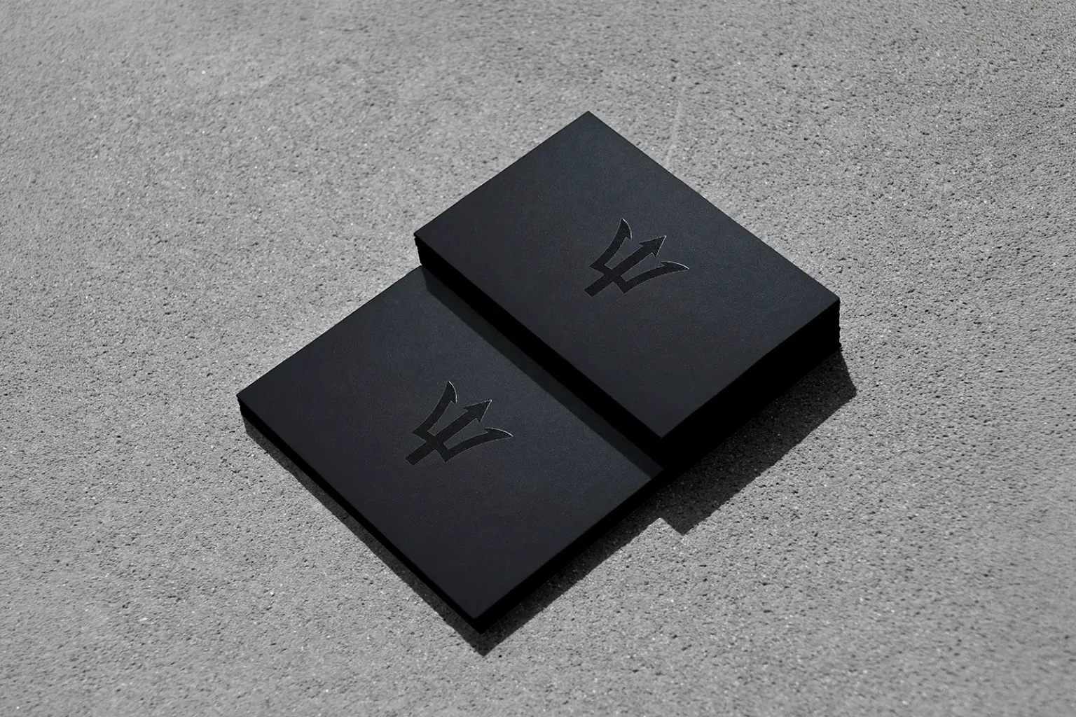 Sophisticated black-on-black business cards with a glossy spot UV trident logo, highlighting the subtle yet luxurious texture of our specialty finishes.