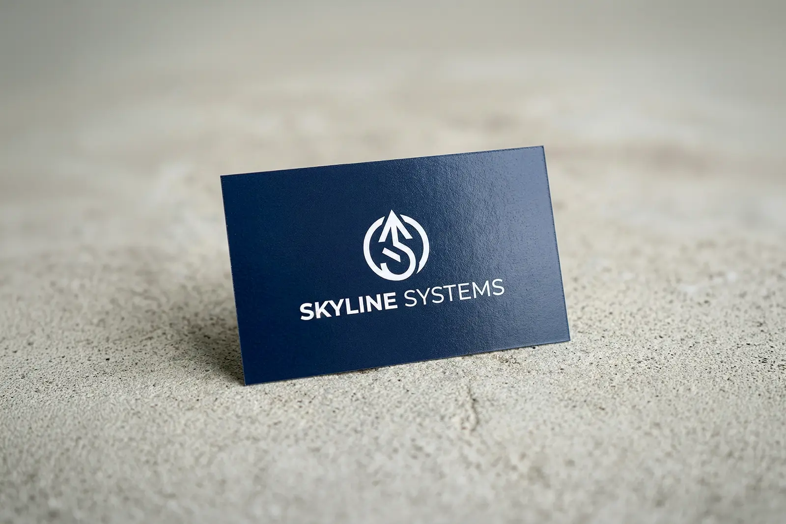 Navy blue Skyline Systems business card with a white logo on a textured concrete surface, highlighting our next-day printing capabilities in New York City.