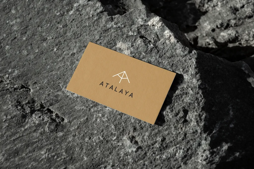 Custom tan-colored business cards for Atalaya displayed on a natural rock surface, highlighting our sharp offset printing and clean design options for everyday professional use.