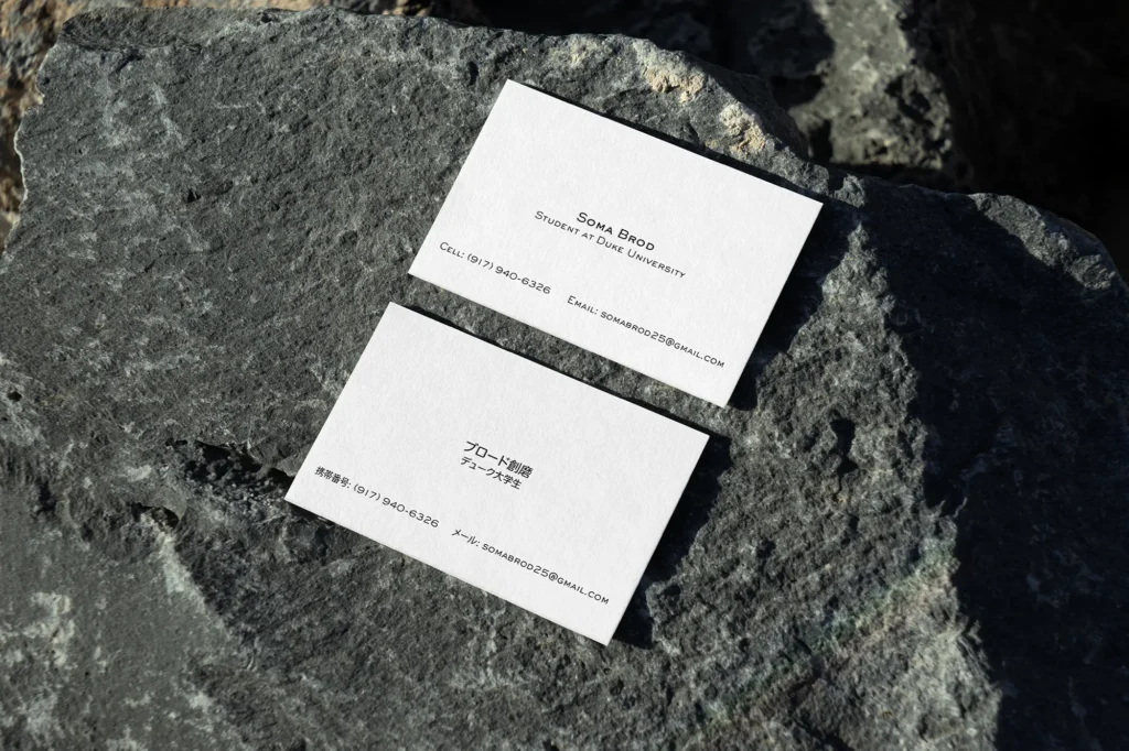 Professional Japanese-English business cards featuring high-fidelity translation and printing, leaning against a rough grey rock surface.