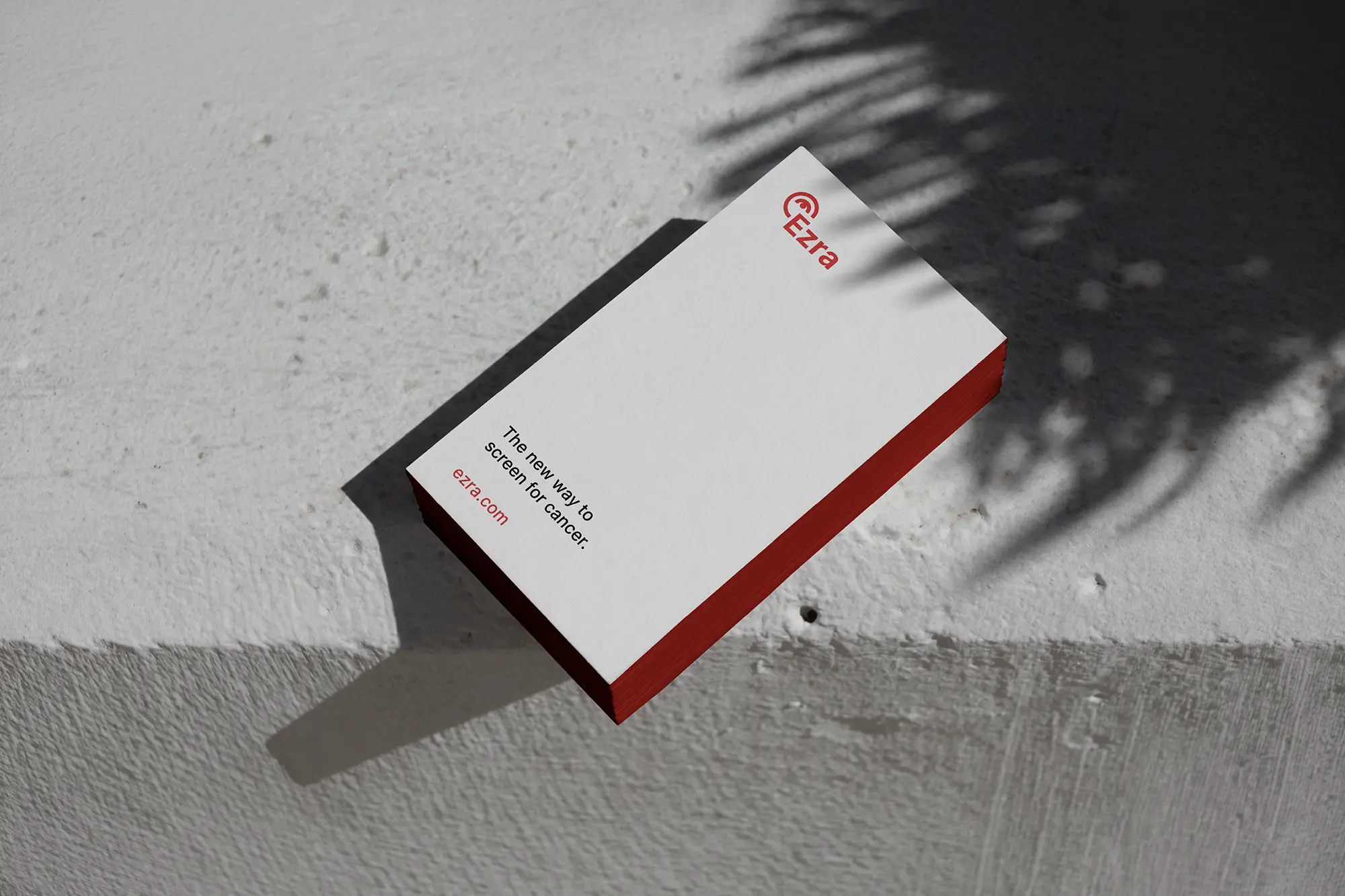 Minimalist white business cards for Ezra featuring striking red painted edges, stacked on a stone surface to emphasize the premium paper thickness.
