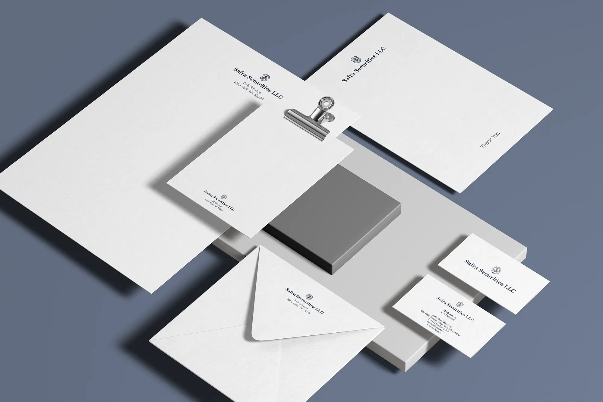 A comprehensive financial stationery suite for Safra Securities LLC, featuring custom letterhead on 24lb Classic Crest and 165lb business cards, crafted in our Manhattan studio and styled on grey architectural blocks against a slate blue background.