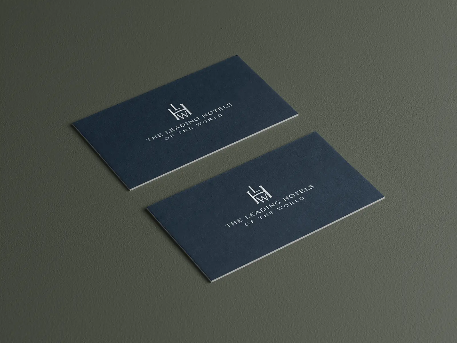 Detailed view of custom navy blue business cards with silver metallic foil accents, styled on a deep olive green surface to highlight the premium tactile finish.